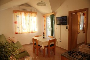 Ein Essbereich mit Tisch, Stühlen, einem an der Wand befestigten Fernseher und einer Küchenzeile mit Gasherd.