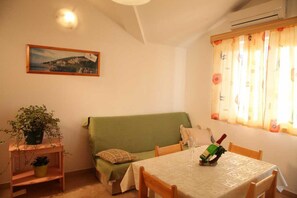 Ein gemütliches Zimmer mit einem grünen Sofa, einem Esstisch mit Stühlen, einer Zimmerpflanze und einem gerahmten Bild an der Wand.