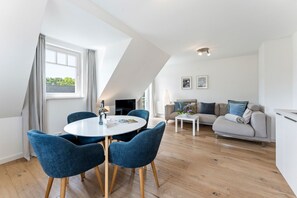 Ein modernes Wohnzimmer mit einem runden Tisch, blauen Stühlen, einer Couch und einem Fernseher.