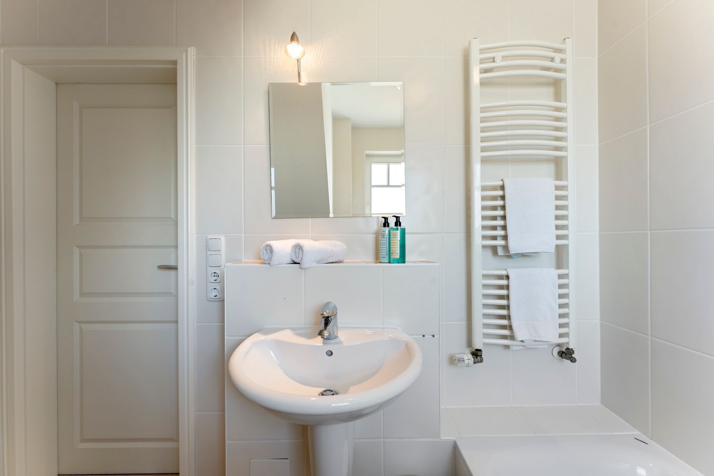 A bathroom with a white sink, mirror, towel rack, and a door.