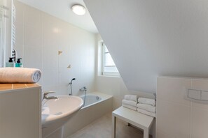 Un baño moderno con lavamanos, bañera y una pequeña mesa con toallas.