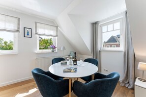 Ein modernes Zimmer mit rundem Tisch, vier Stühlen, einem Fenster mit Aussicht, einem Heizkörper und einer Lampe.