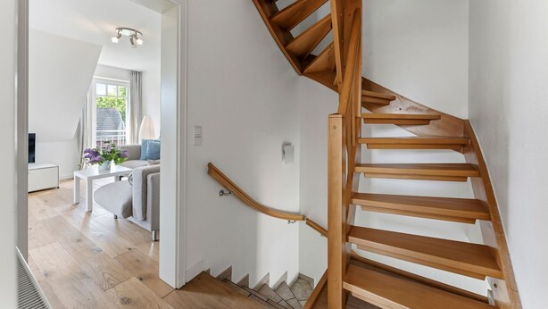 A wooden staircase in a modern interior with a white wall and a door leading to a living area with a sofa and a table. - Conwind 2 - House Conwind. - Apartment 2 (78 m²). In Keitum for up to 4 people (Sylt)