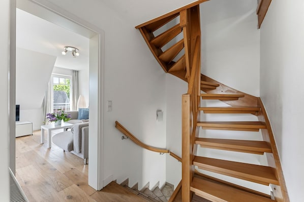 A wooden staircase in a modern interior with a white wall and a door leading to a living area with a sofa and a table. - Conwind 2 - House Conwind. - Apartment 2 (78 m²). In Keitum for up to 4 people (Sylt)