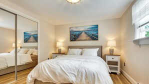 Een slaapkamer met een bed, nachtkastjes, een schilderij en een raam.