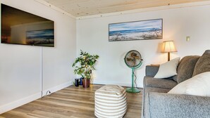 Een woonkamer met een flatscreen televisie, een schilderij, een ventilator, een bank en een potplant.