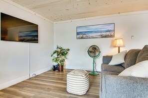 Ein Wohnzimmer mit Flachbildfernseher, einem Gemälde, einem Ventilator, einer Couch und einer Topfpflanze.