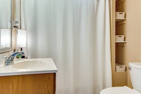 A bathroom with a white sink, mirror, and shower curtain. There are storage shelves above the toilet. - Walk to Wells Beach! Family-Friendly Gem w/ Patio (Wells)