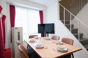 Quarto de hotel com uma mesa de jantar posta para quatro pessoas, uma televisão, um guarda-roupa e uma escadaria.