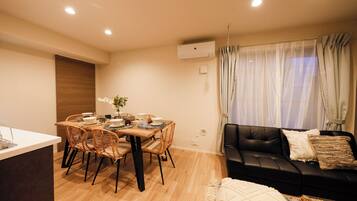 Una sala moderna con un sofá de cuero negro, una mesa de comedor con sillas de mimbre y un ventanal con cortinas traslúcidas.