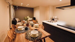 Un comedor con una mesa de madera dispuesta para cuatro, rodeada de sillas de mimbre. Se ve una cocina a la derecha, con una encimera y un lavabo blancos.