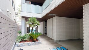 Un edificio moderno con un área exterior cubierta, un balcón y un pequeño jardín con plantas.