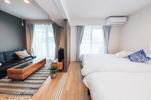 Quarto de hotel moderno com sofá, cama, televisão e planta em vaso.