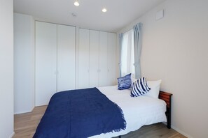 A bedroom with a bed, a blue blanket, white bedding, and a wooden headboard. - Pacific Coast Enoshima by Teranova 2 (Fujisawa)