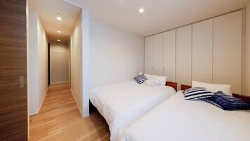 A hotel room with a wooden floor, a bed with white bedding, a wardrobe, and a hallway leading to another room.