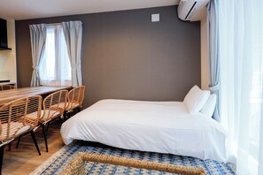 Un dormitorio con cama, una mesa de comedor con sillas y una ventana con cortinas.