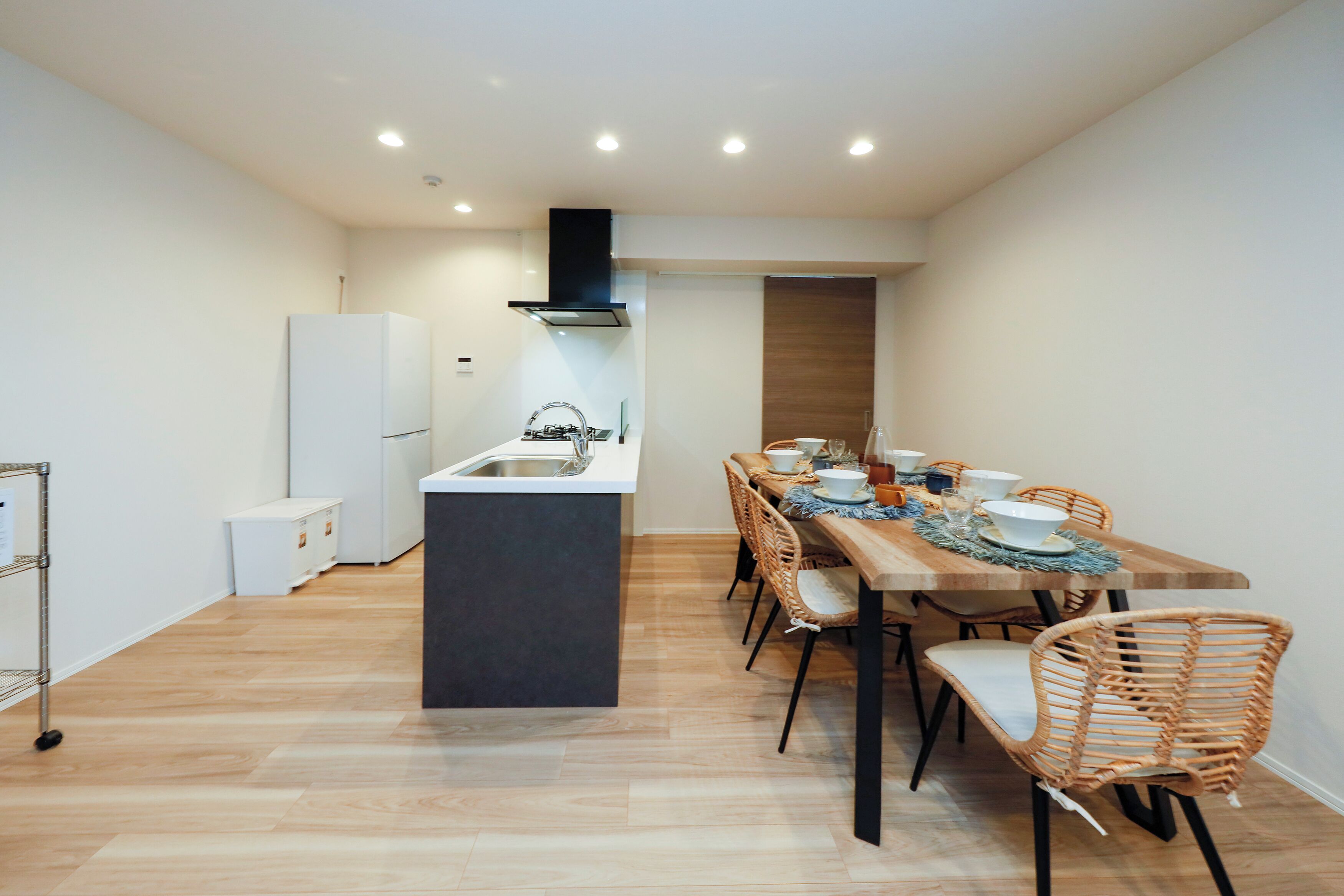 A compact kitchen with a central island, a dining area with wicker chairs, and a white refrigerator.