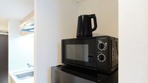 Microondas negra compacta con cafetera encima, sobre un refrigerador de acero inoxidable en una cocina moderna.