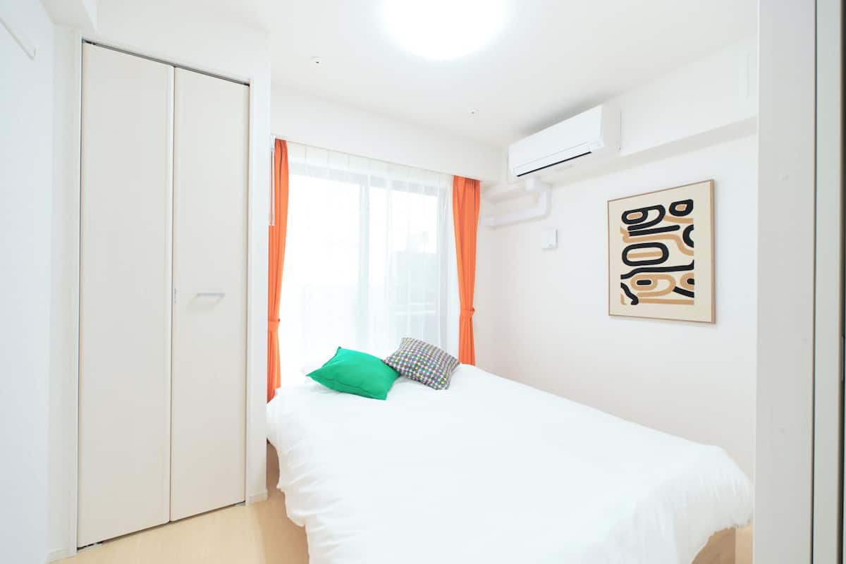 A bedroom with a bed, a wardrobe, an air conditioning unit, and a window with curtains.