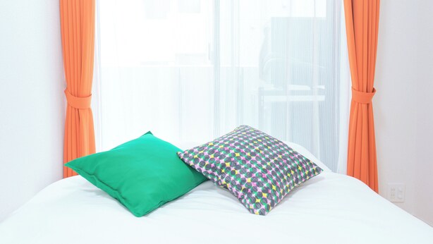 Una cama con dos almohadas, una ventana con cortinas y una pared blanca.