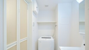 Un baño compacto con paredes blancas, lavadora y secadora integradas, un estante pequeño y un espejo.
