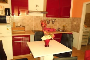 A compact kitchen with red cabinets, a microwave, a sink, and a dining table with chairs. - Sea View Apt with Terrace Kitchen (Opatija)