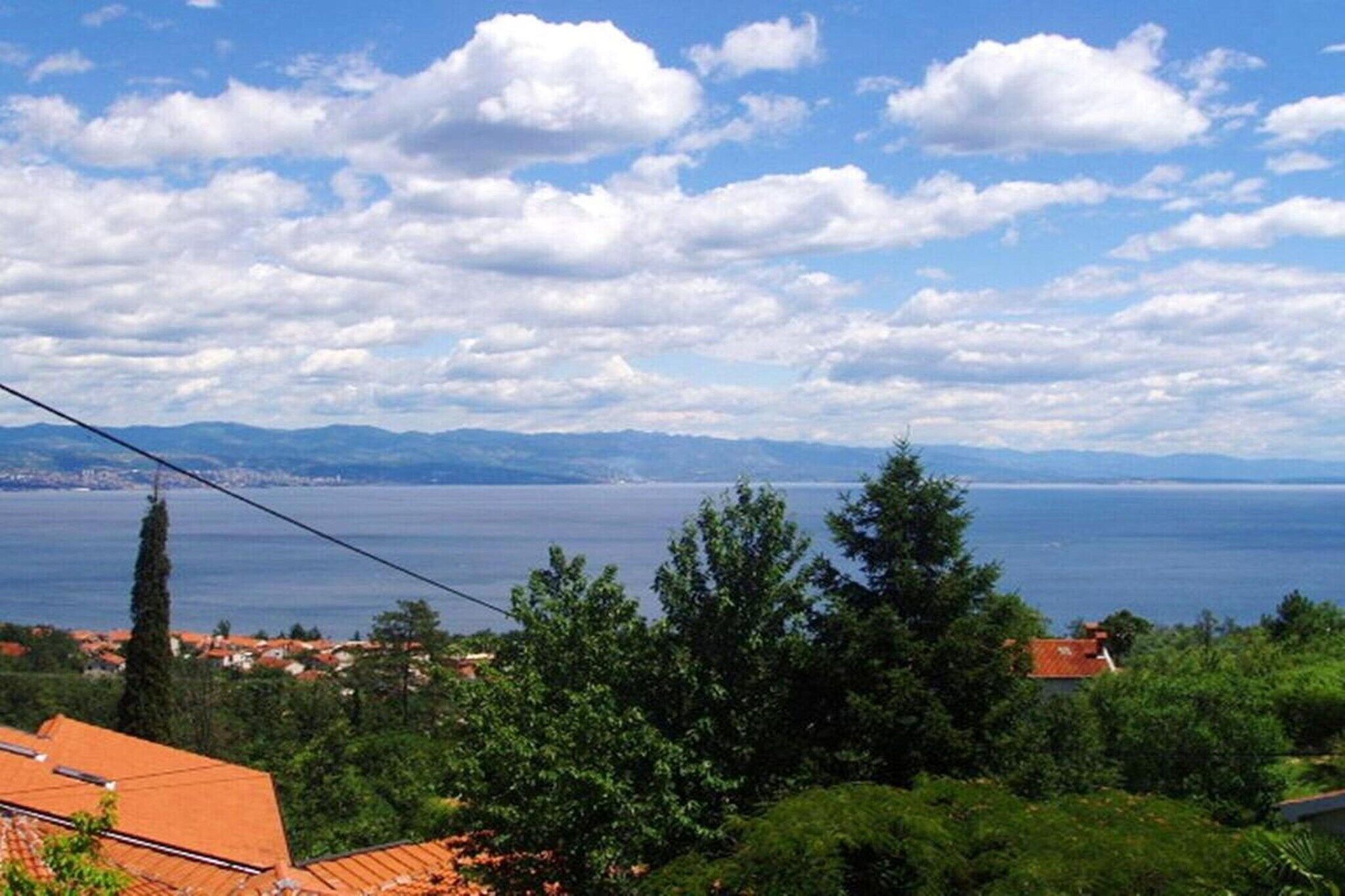 Eine Küstenlandschaft mit Blick auf das Meer, Berge im Hintergrund und Wohnhäuser mit roten Ziegeldächern.