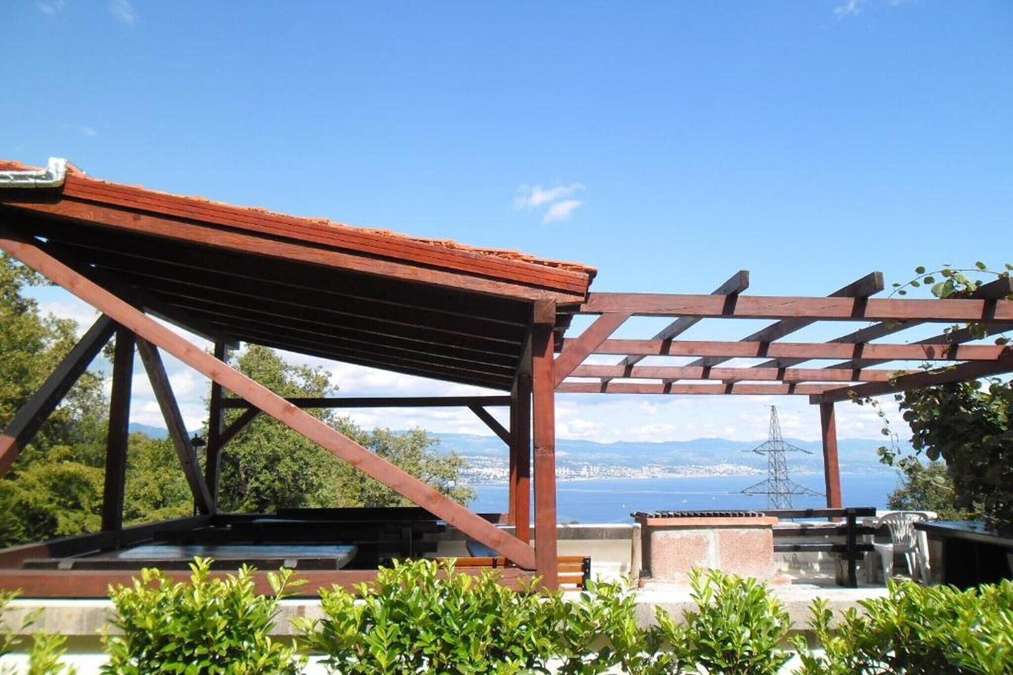 Une pergola en bois offrant une vue sur la mer et sur un pylône de ligne électrique.