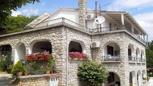 Un edificio de piedra con varios balcones, plantas en macetas y mesas al aire libre.
