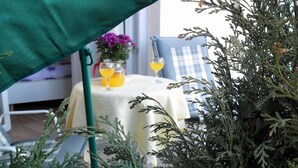 Una mesa con mantel blanco, dos vasos de jugo de naranja y un jarrón con flores moradas.