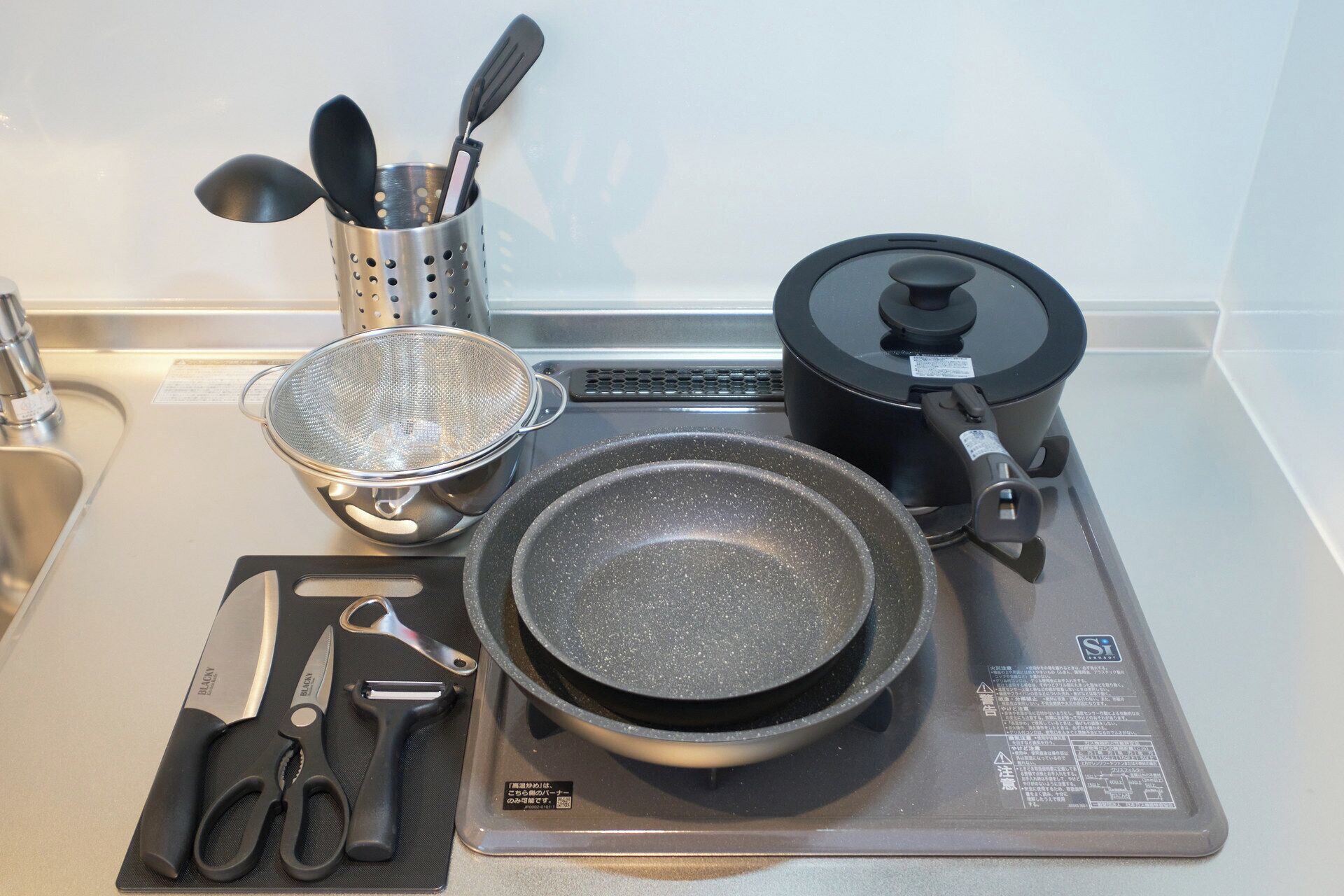 A kitchen with a stove, a frying pan, a colander, a spatula, a pair of scissors, and a knife.