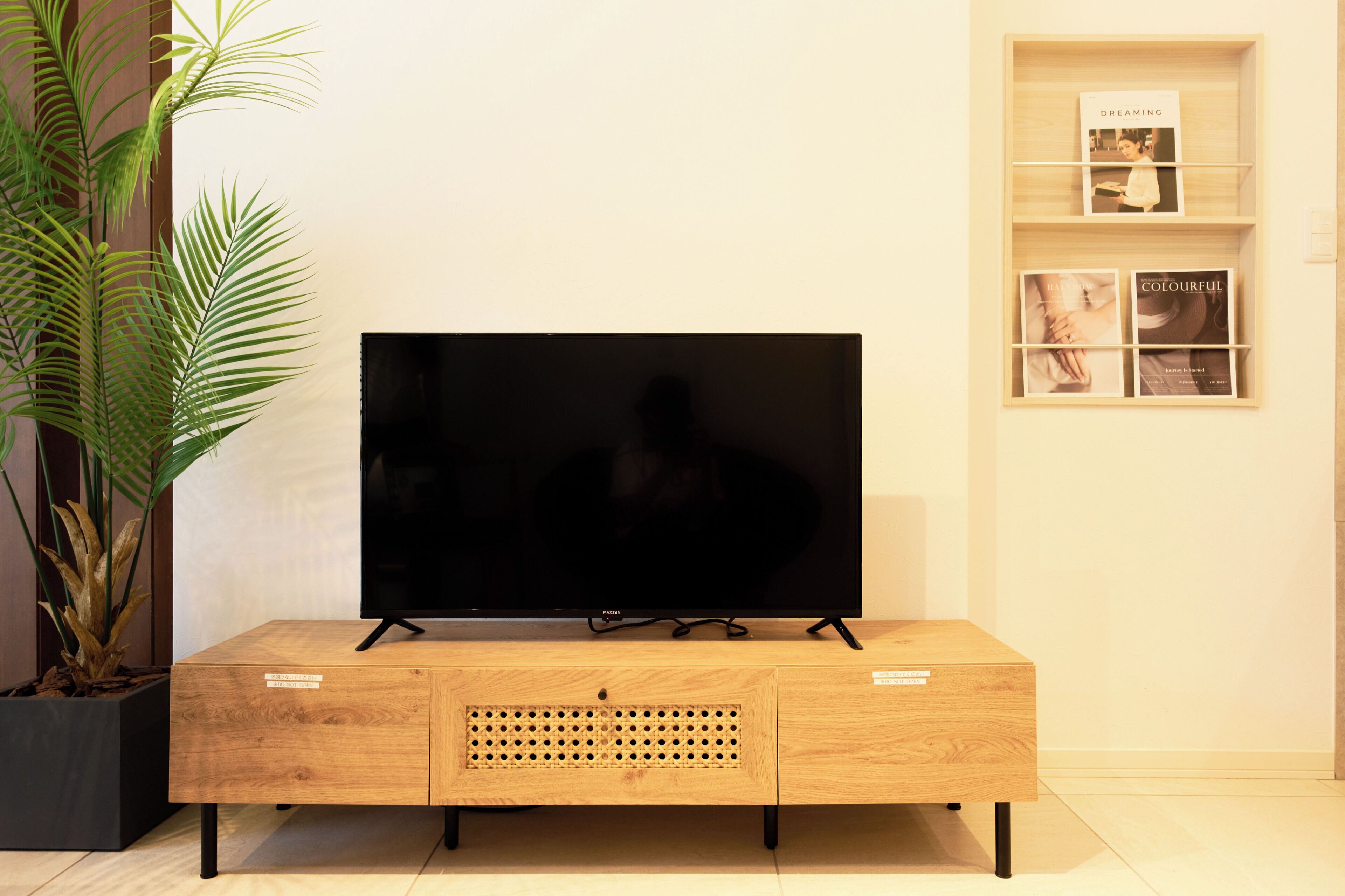 Ein Flachbildfernseher auf einer Holzkommode mit einem Regal darüber, auf dem Bücher und ein gerahmtes Foto stehen.
