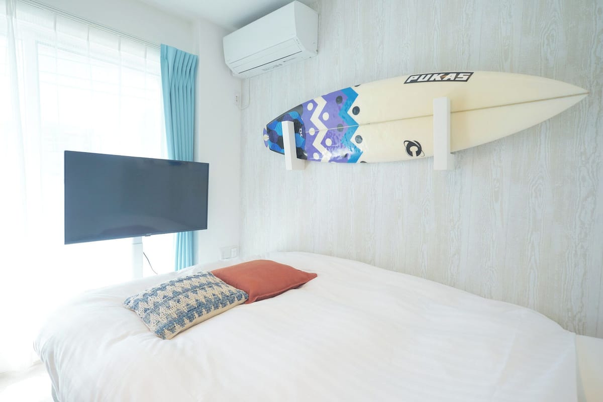 A bedroom with a bed, a mounted TV, and a surfboard on the wall.