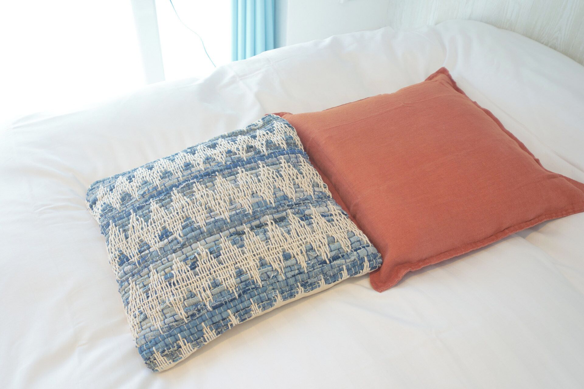 Un lit avec des draps blancs et deux oreillers, l’un à motifs bleus et blancs et l’autre d’un rouge uni.