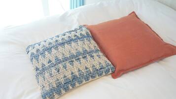 Un lit avec des draps blancs et deux oreillers, l’un à motifs bleus et blancs et l’autre d’un rouge uni.