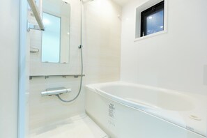 Ein modernes Badezimmer mit einer weißen Badewanne, einer Duschkabine aus Glas und einem kleinen Fenster.
