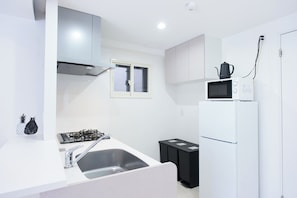 A modern kitchen with white cabinetry, a gas stove, a sink, a microwave, and a refrigerator. - Creare Togoshi Ginza by Tranova  2 (Tokyo)