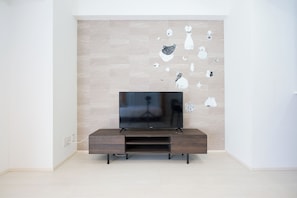 Ein modernes Wohnzimmer mit Fernseher an einer Holzvitrine, einer hell gefliesten Wand und minimalistischer Einrichtung.