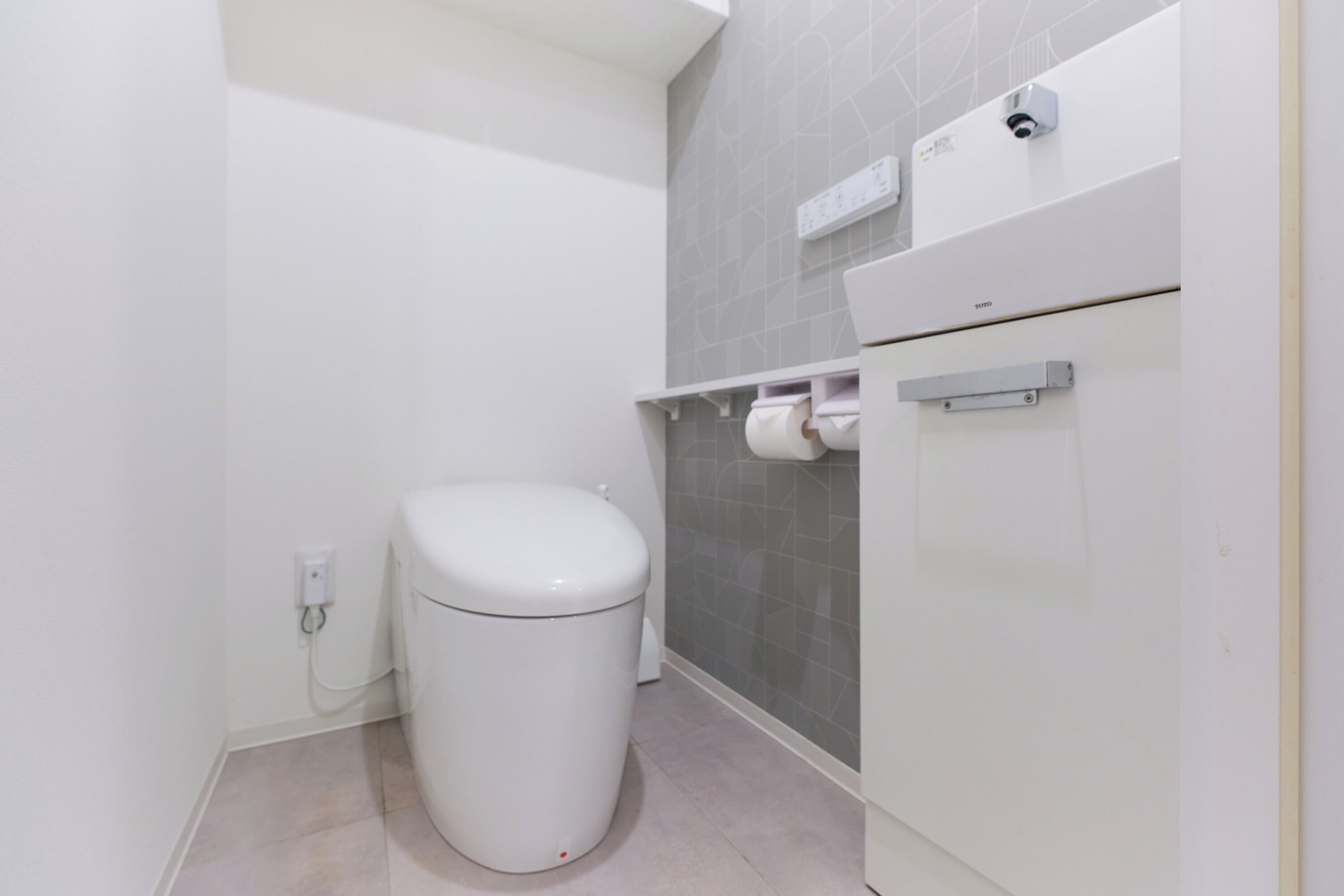 Een kleine, moderne badkamer met toilet, een handdoekdispenser en een beveiligingscamera.