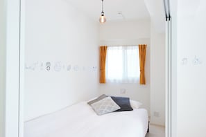 Ein Schlafzimmer mit Bett, einem Fenster mit Vorhängen, einer Wand mit Zeichnungen und einer Hängelampe.