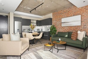 A modern living room with a sofa, coffee table, and a dining area with chairs. - The Signature | Designer De Waterkant Retreat (Cape Town)