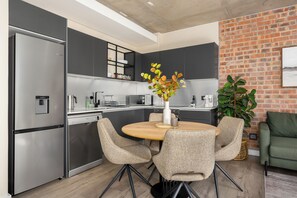 A modern kitchen with a dining area, stainless steel appliances, and a brick wall. - The Signature | Designer De Waterkant Retreat (Cape Town)