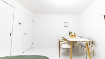 A minimalist room with a bed, a dining table with chairs, and a small kitchenette area.