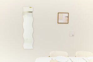 Ein Zimmer mit weißer Wand, einem gerahmten abstrakten Gemälde, einer weißen Klimaanlage und einem Tisch, gedeckt mit Tellern, Besteck und Gläsern.