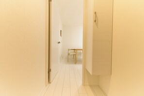 Un pasillo estrecho con paredes blancas y piso de baldosas que conduce a una habitación con cama y sillón.