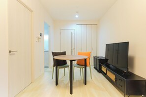 Ein Zimmer mit Fernseher, einem Tisch, zwei Stühlen und einem Kleiderschrank.