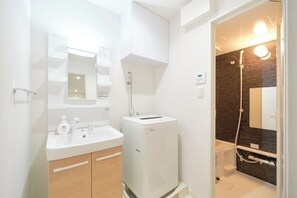Ein modernes Badezimmer mit einem weißen Waschbecken, einem Spiegel und einer Duschkabine mit dunklen Fliesen.