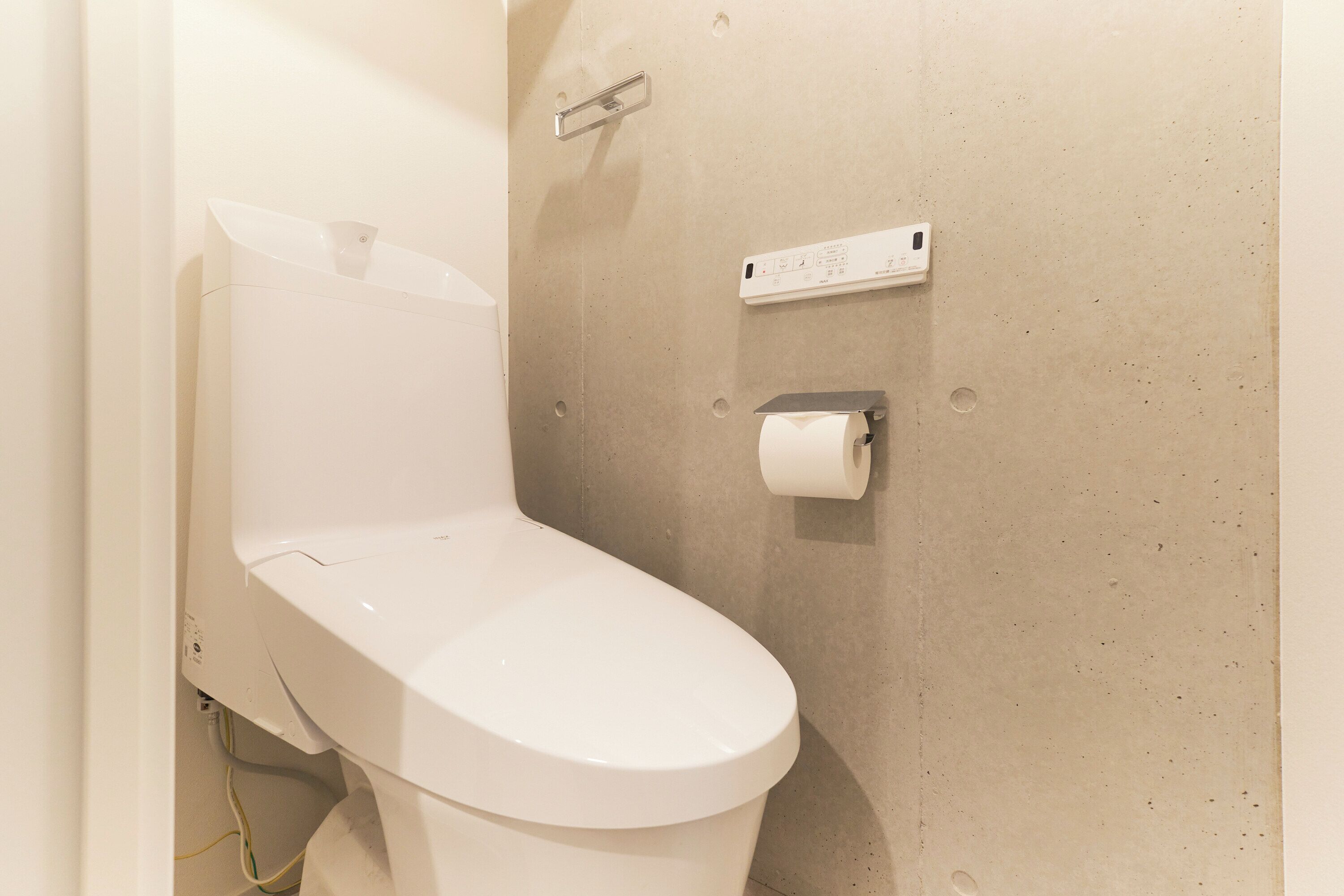 Un inodoro blanco con el sistema de descarga empotrado en la pared y dispensador de toallas de papel.