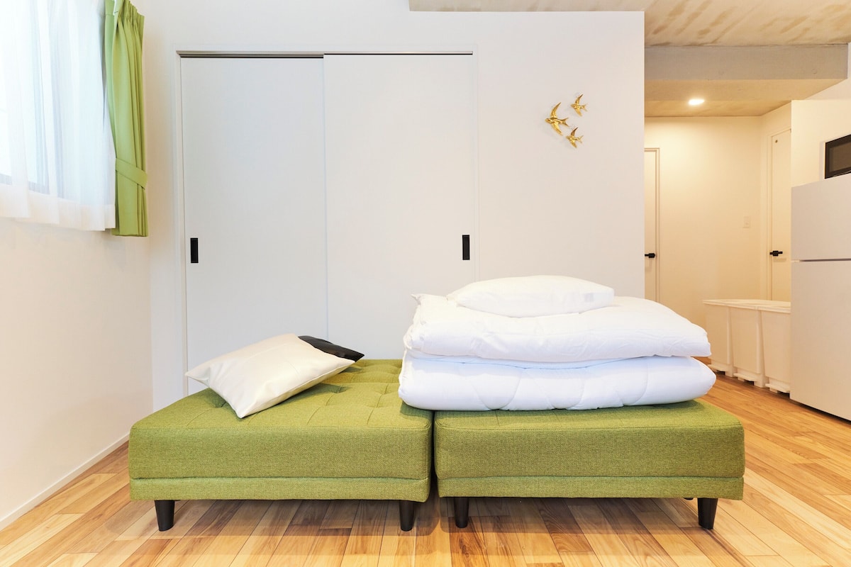 A room with two green ottomans, a white door, and a white wall with a gold decoration.