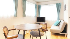 A room with a round table, two chairs, a sofa, a television, and curtains on the windows. - FrontierComfortKitaIkebukurobyTranova 2 (Toshima City)